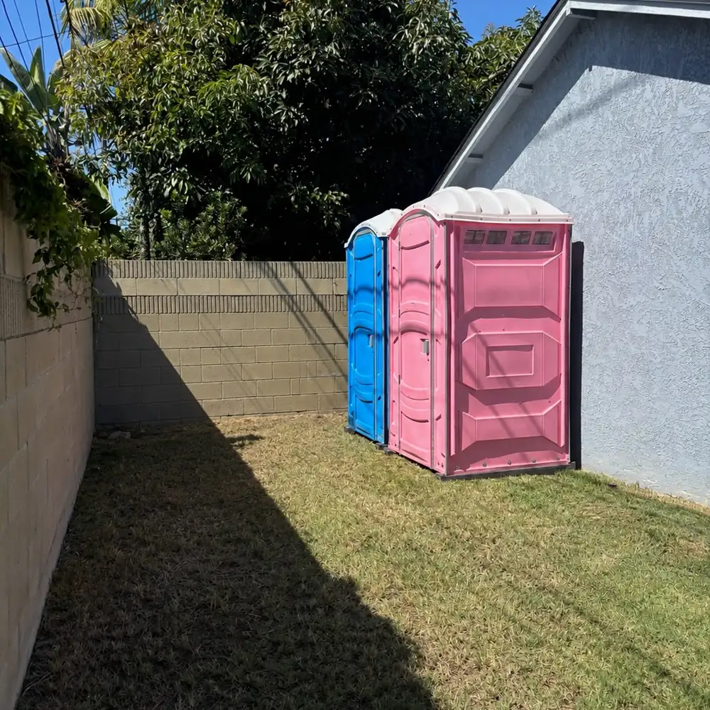 Blue and pink porta potties set beside a backyard fence for a party