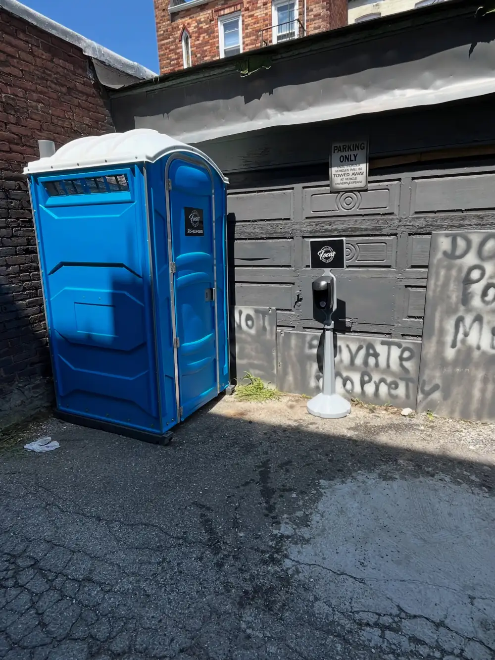 Single blue porta potty placed beside a driveway gate