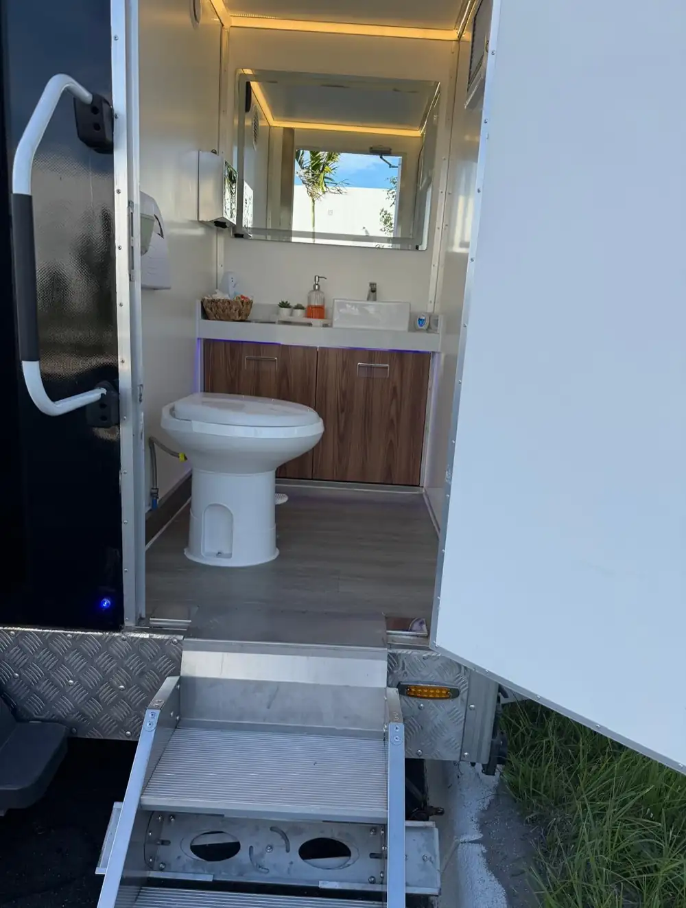 Lit restroom trailer stall with toilet and wood vanity
