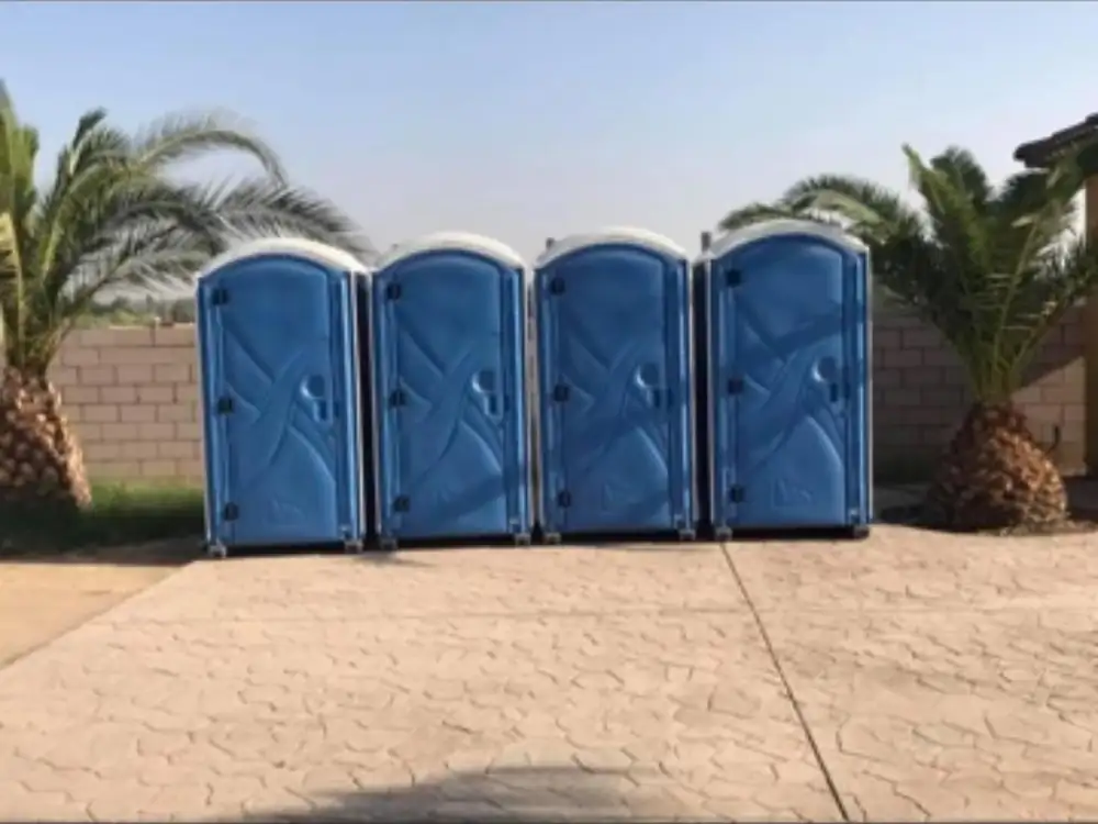 Four blue standard porta potties lined up on a paved driveway