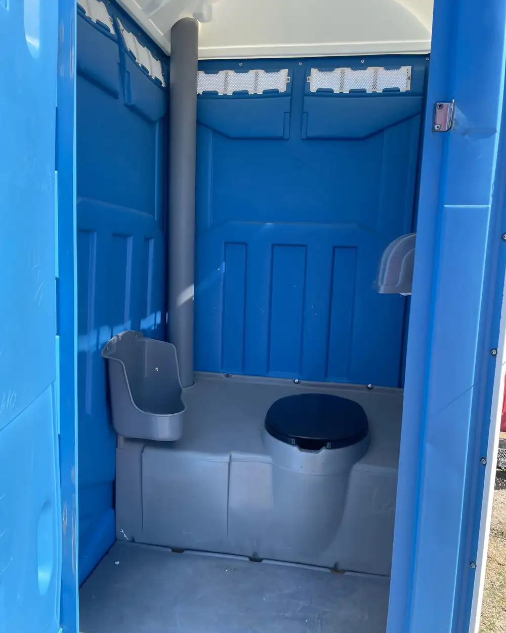 Inside a blue standard porta potty showing seat, urinal and paper holder